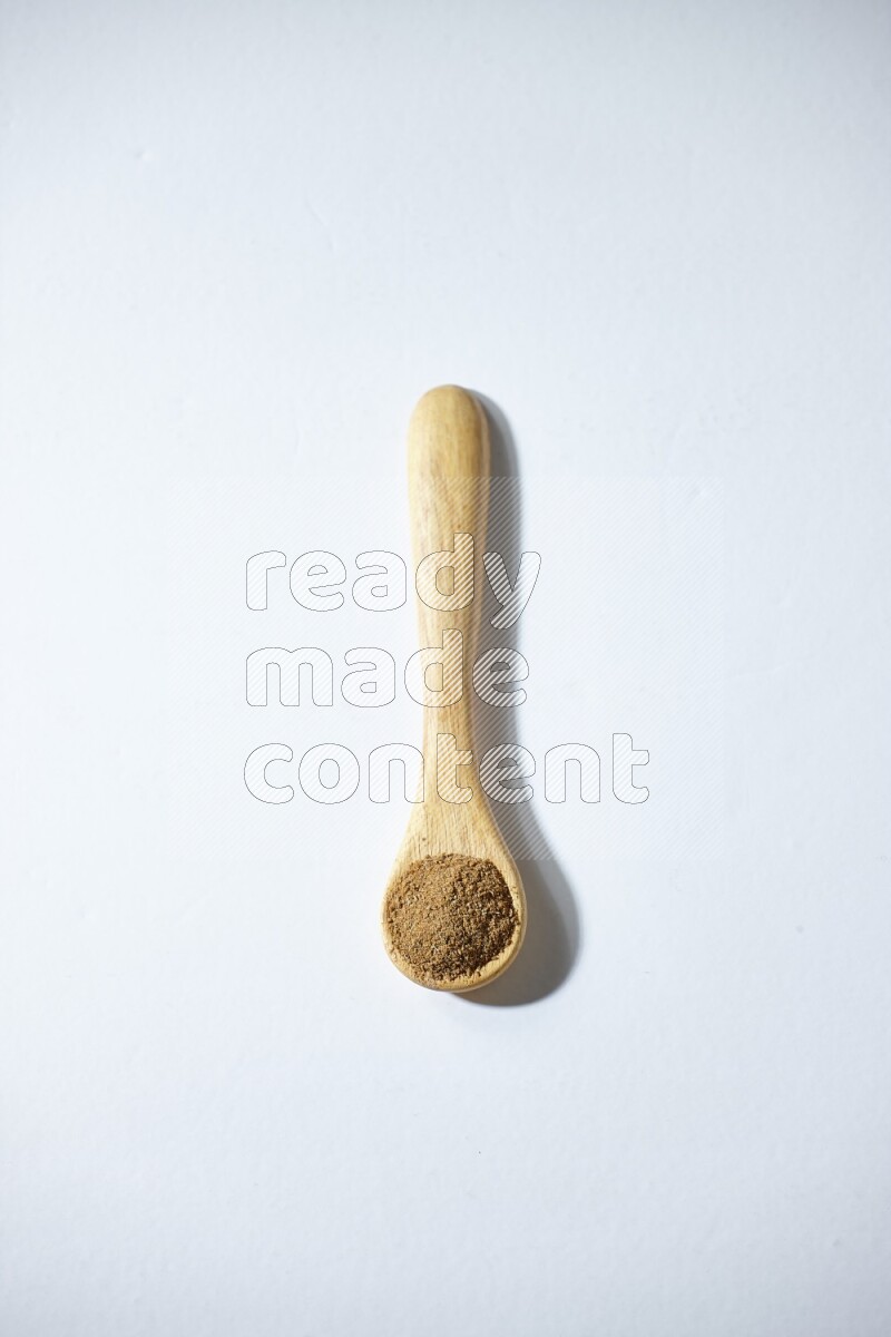A wooden spoon full of cumin powder on a white flooring
