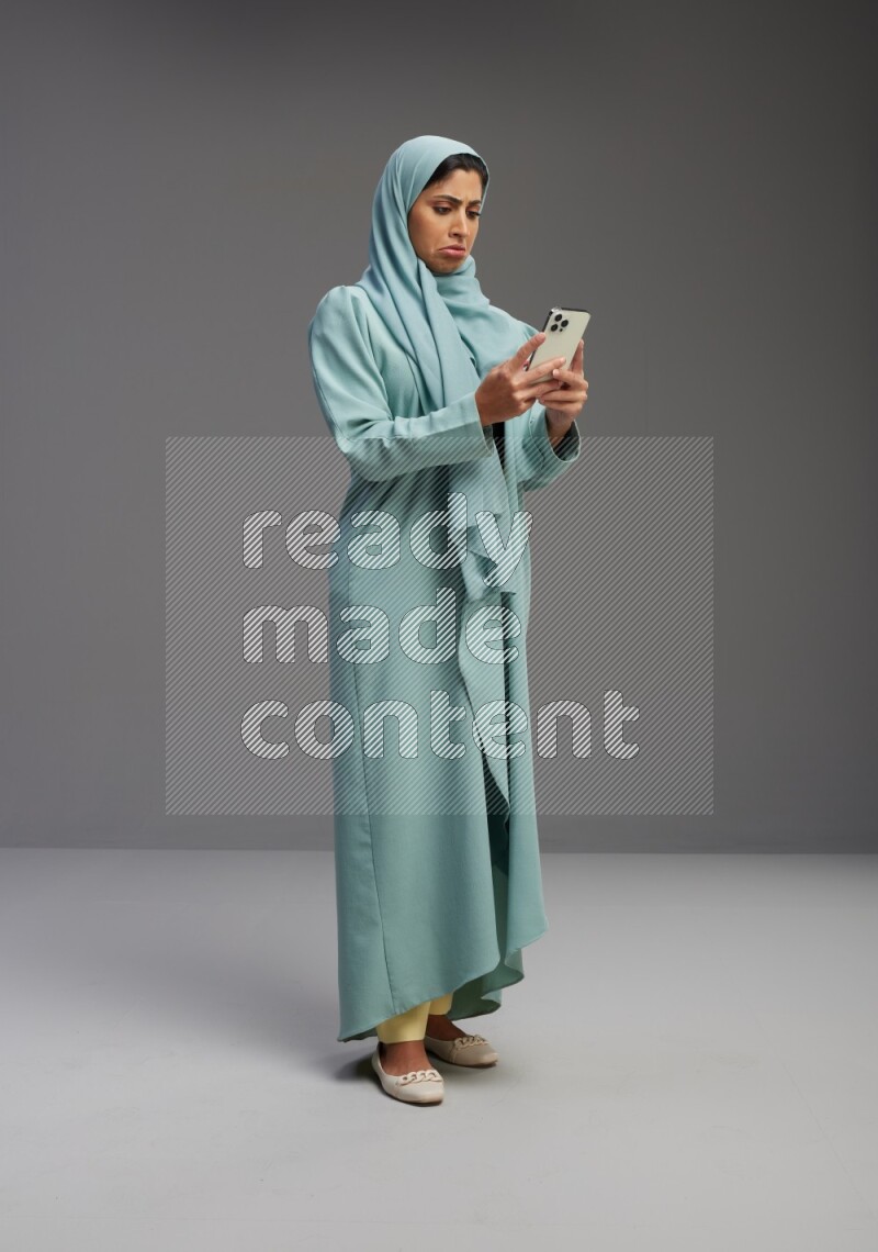 Saudi Woman wearing Abaya standing texting on phone on Gray background