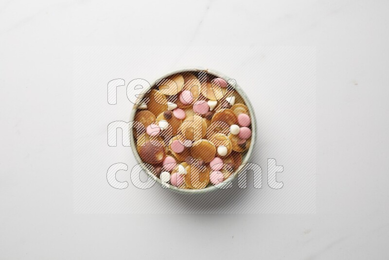Top-view shot of mixed chocolate chips cereal pancakes in a round bowl on white background
