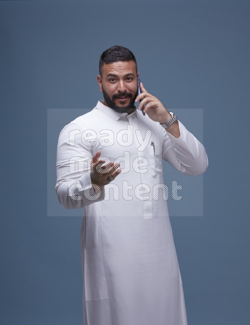 A Saudi man calling on blue background wearing Saudi Thob