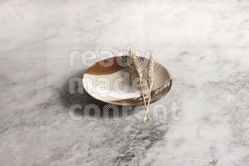 Wheat stalks on multicolored pottery plate on grey marble background
