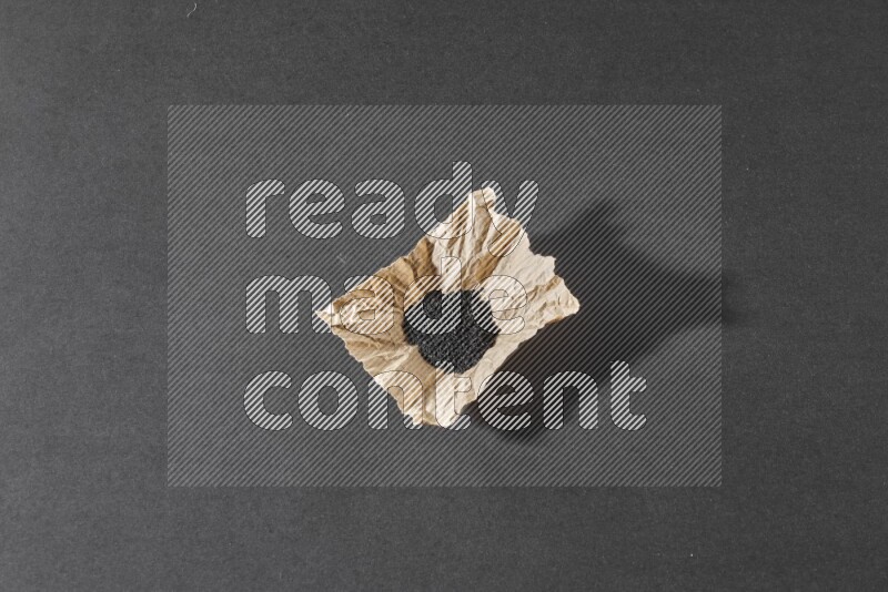 A crumpled piece of paper full of black seeds on a black flooring