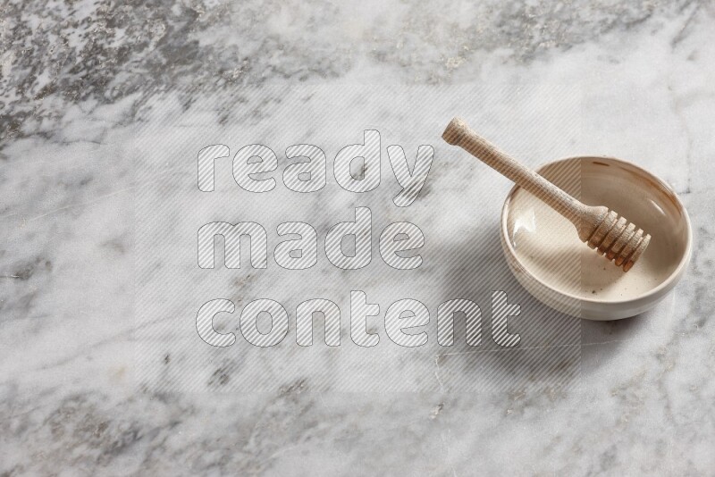 Beige pottery bowl with wooden honey dipper in it on grey marble background