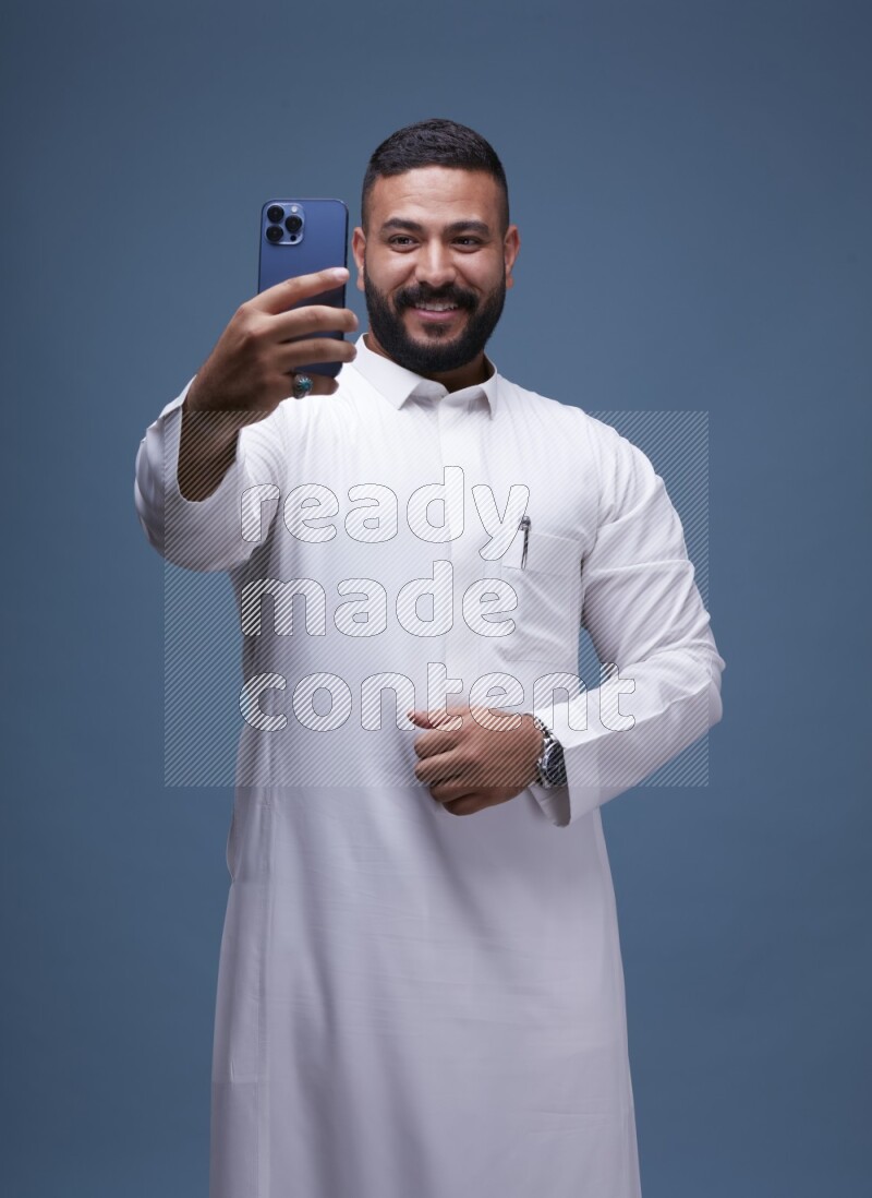 A Saudi man Taking A Selfie on Blue Background wearing Saudi Thob