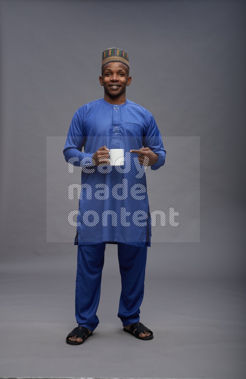 Man wearing Nigerian outfit standing holding mug on gray background
