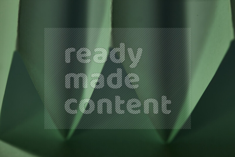A close-up abstract image showing sharp geometric paper folds in green gradients