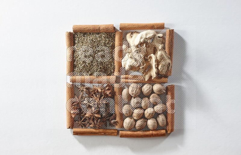 4 مربعات من أعواد القرفة ممتلئة باليانسون والزنجبيل والكمون وجوزة الطيب على أرضية بيضاء