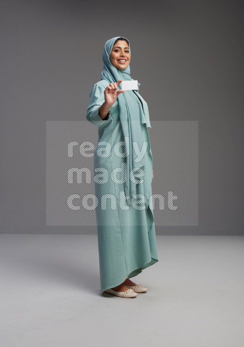 Saudi Woman wearing Abaya standing holding ATM card on Gray background