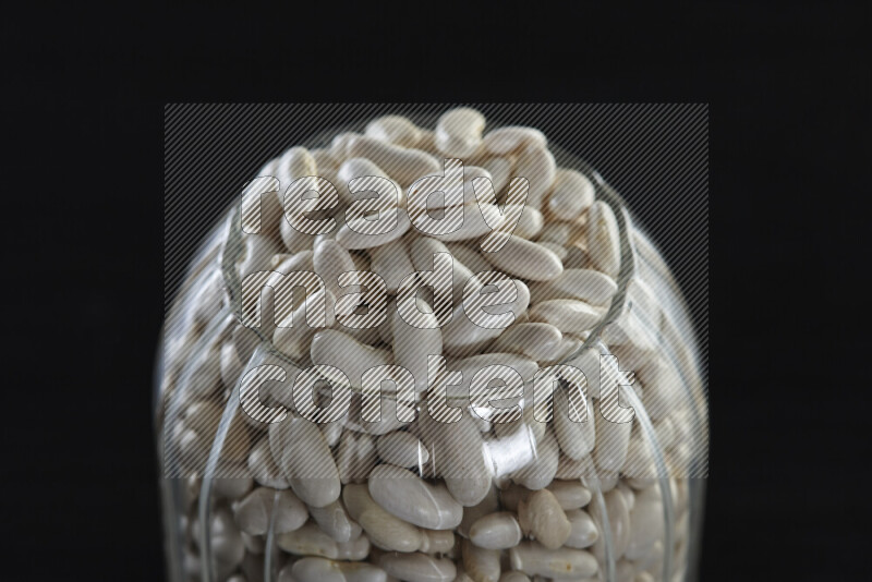 White beans in a glass jar on black background