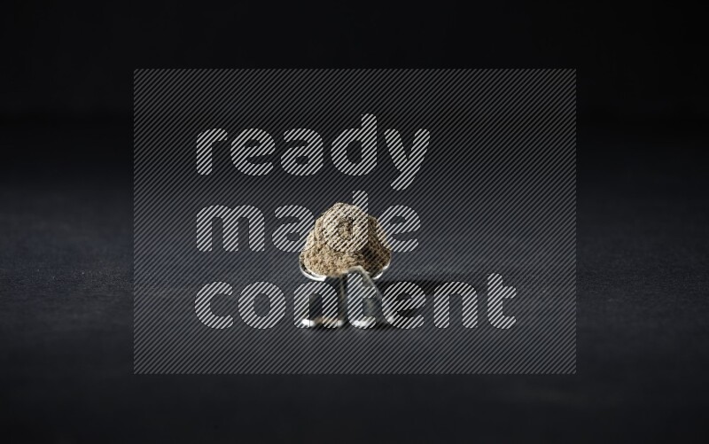 2 Metal spoons full of cardamom powder on black flooring