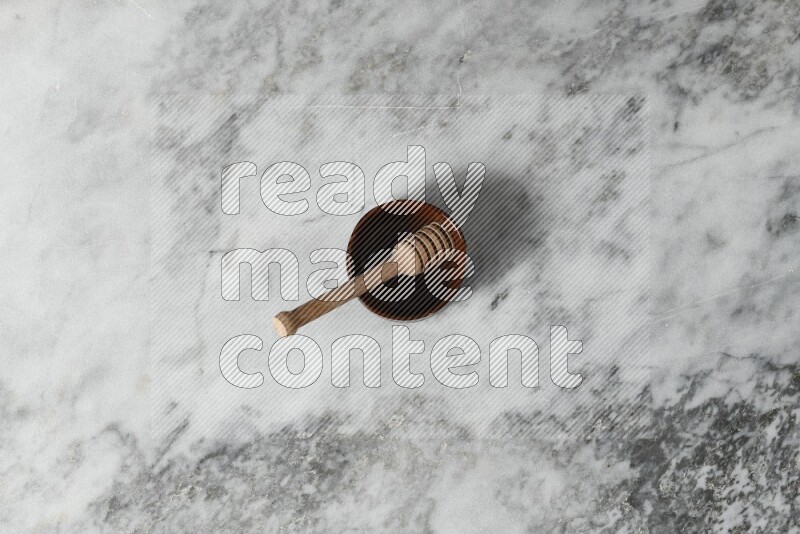 Brown pottery bowl with wooden honey dipper in it on grey marble background