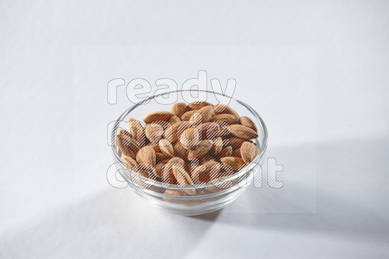 A glass bowl full of peeled almonds on a white background in different angles