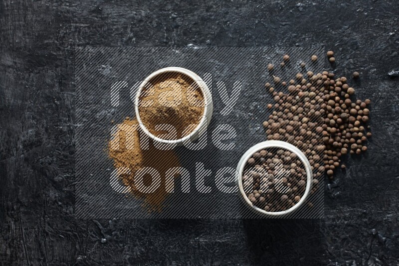 2 beige bowls, one full of allspice powder and the other full of whole balls and both spread on a textured black flooring