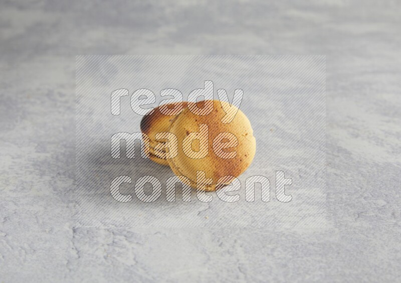 45º Shot of two Yellow Crème Brulée macarons on white  marble background