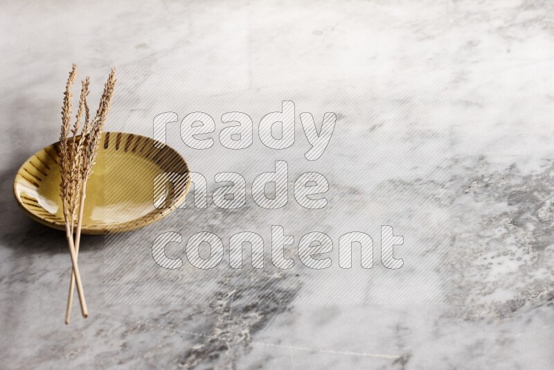 Wheat stalks on multicolored pottery plate on grey marble background