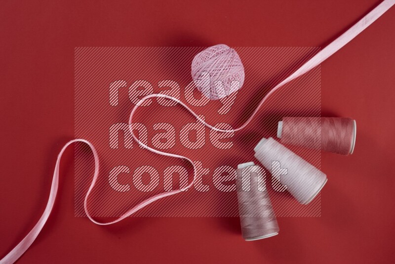 A pink and red collection of sewing and tailoring tools arranged on a red background
