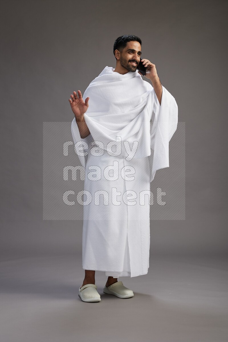 A man wearing Ehram Standing talking on phone on gray background