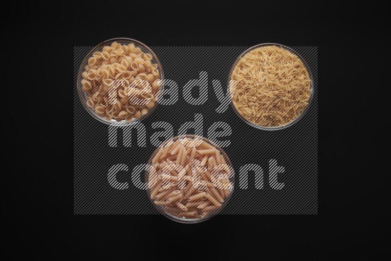 Different pasta types in glass bowls on black background