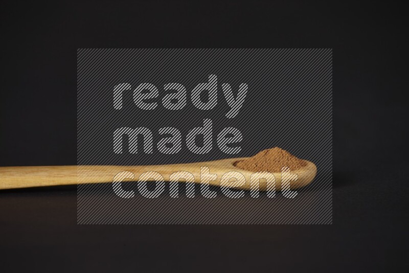 Cinnamon powder in a wooden spoon on a black background