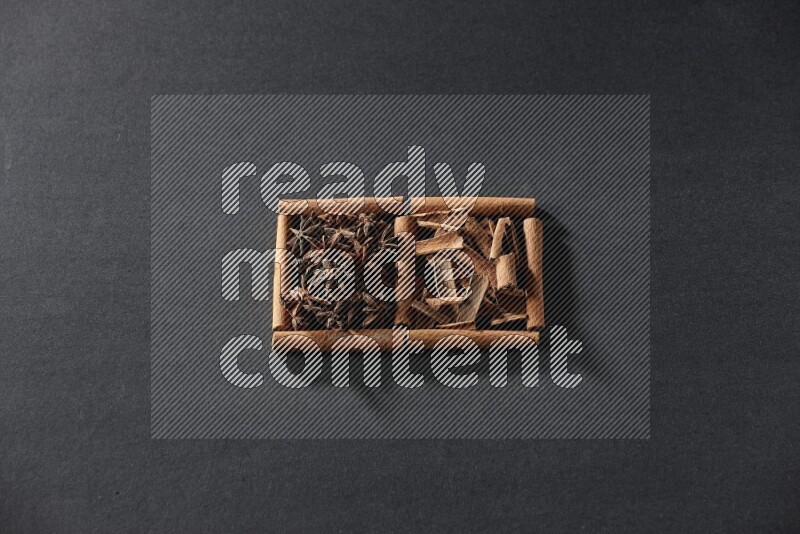 مربعان من أعواد القرفة ممتلئان باليانسون النجمي وقطع من القرفة علي خلفية سوداء