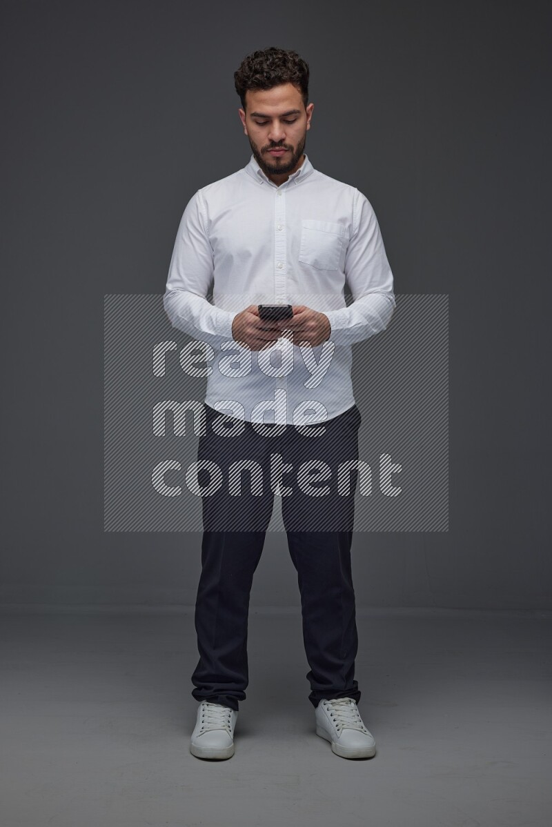 A man wearing smart casual standing and using his phone eye level on a gray background