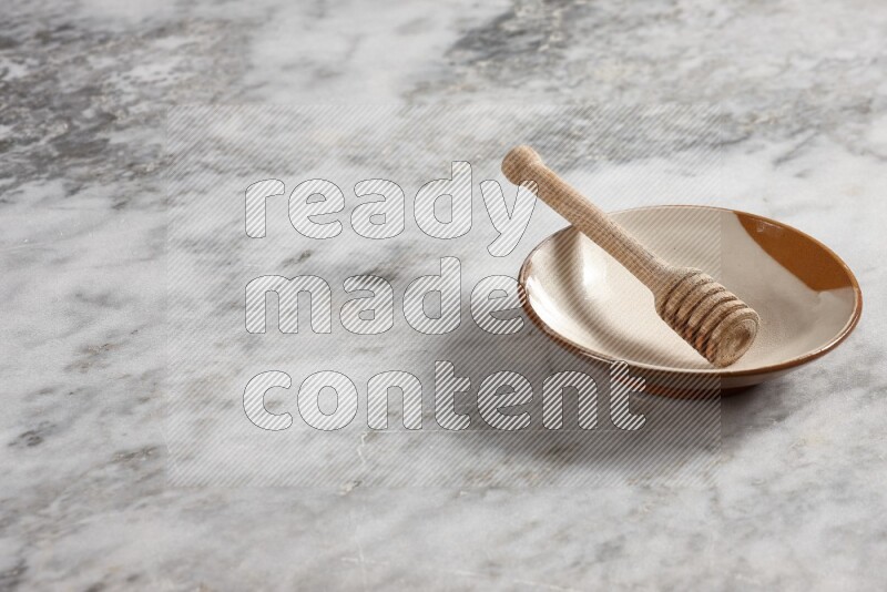 Multicolored pottery plate with wooden honey dipper in it on grey marble background