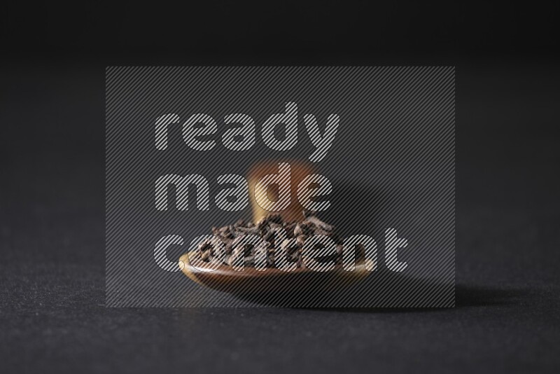 A wooden ladle full of whole cloves on a black flooring