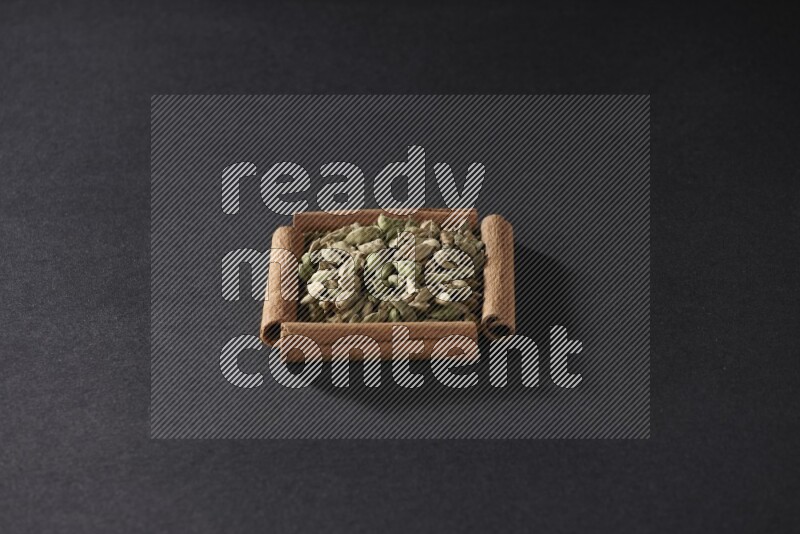 أربعة من أعواد القرفة مكونة شكل مربع بداخلها حبوب الهيل علي خلفية سوداء