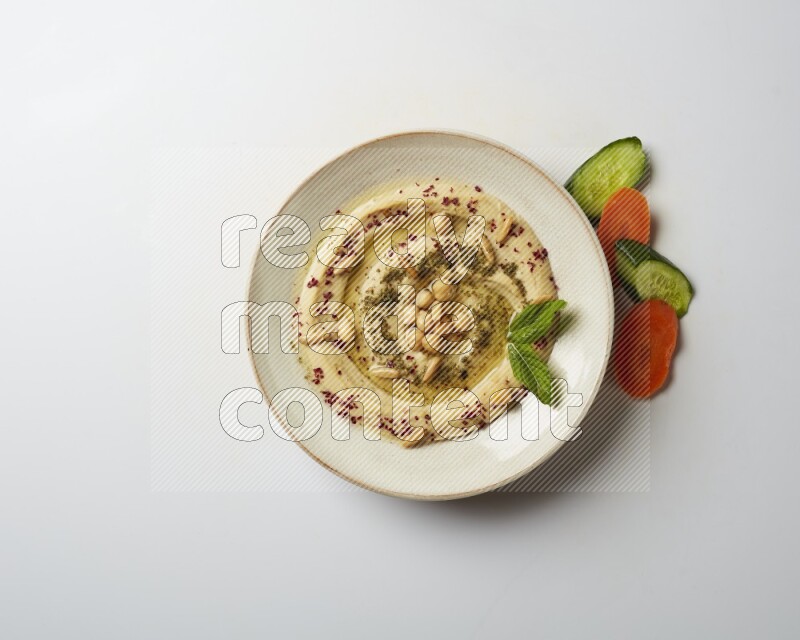 Hummus in a pottry plate garnished with zaatr & sumak on a white background
