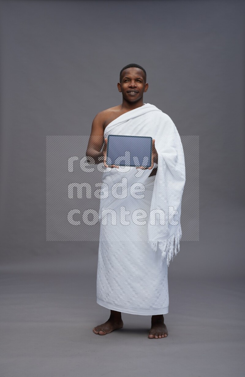 A man wearing Ehram Standing showing tablet to camera on gray background