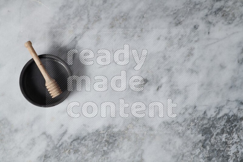 Black pottery oven plate with wooden honey dipper in it on grey marble background
