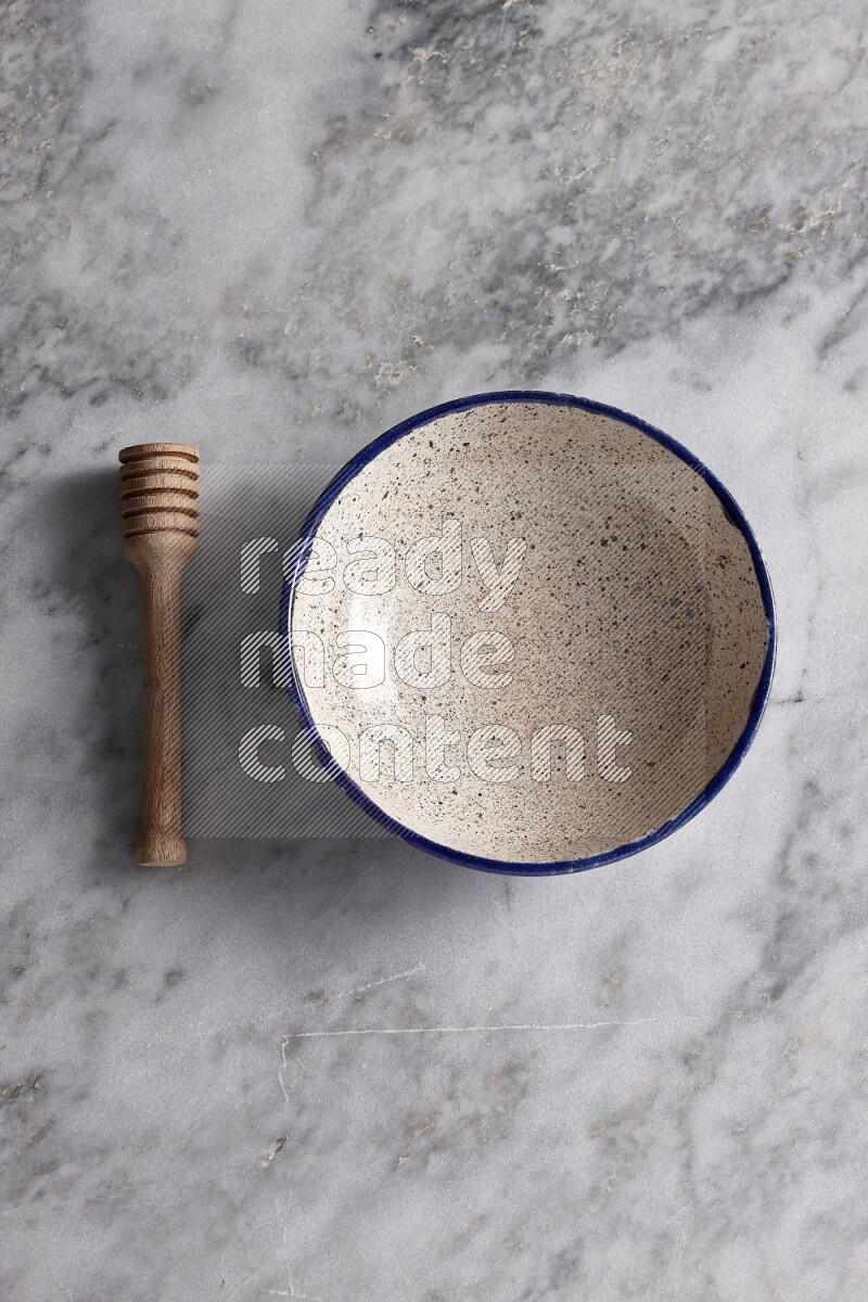 Multicolored pottery bowl with wooden honey dipper on the side on grey marble background