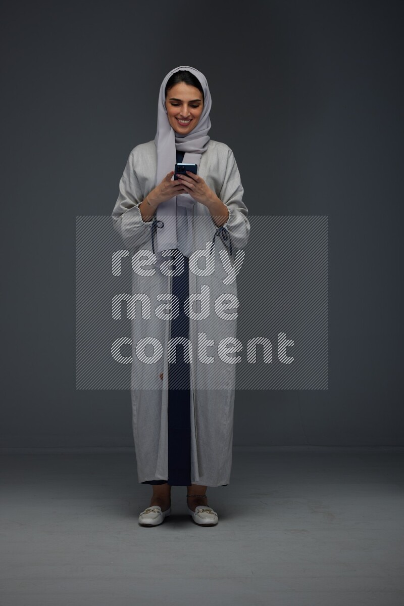 A Saudi woman Texting wearing Grey Abaya on a grey background