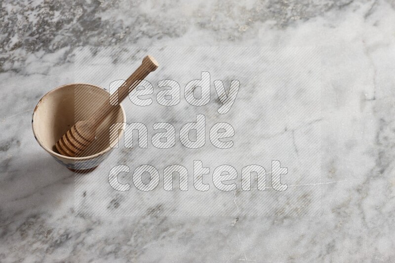 Beige pottery bowl with wooden honey dipper in it on grey marble background