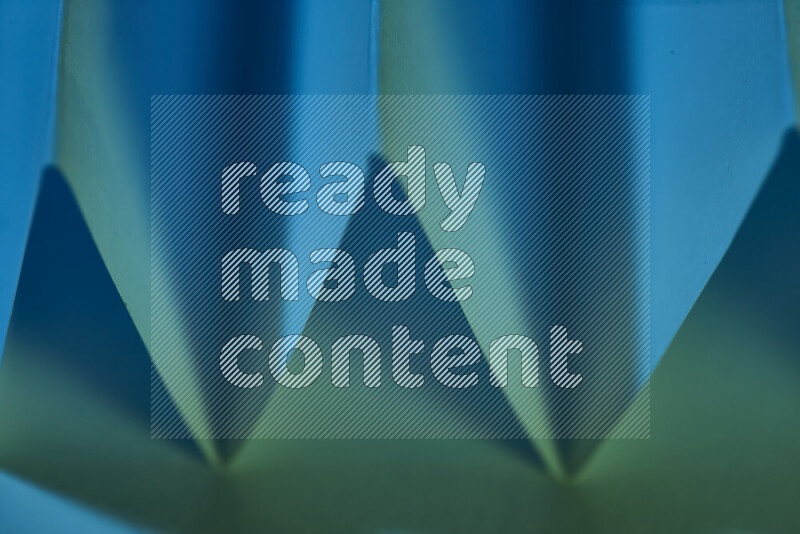 A close-up abstract image showing sharp geometric paper folds in green and blue gradients