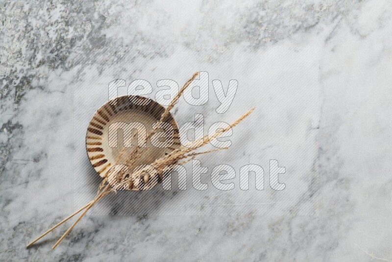 Wheat stalks on multicolored pottery plate on grey marble background