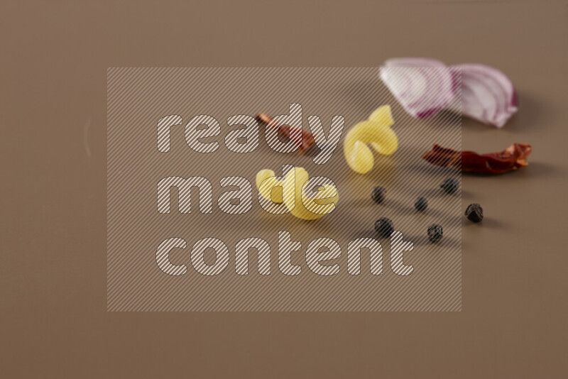 Raw pasta with different ingredients such as cherry tomatoes, garlic, onions, red chilis, black pepper, white pepper, bay laurel leaves, rosemary and cardamom on beige background