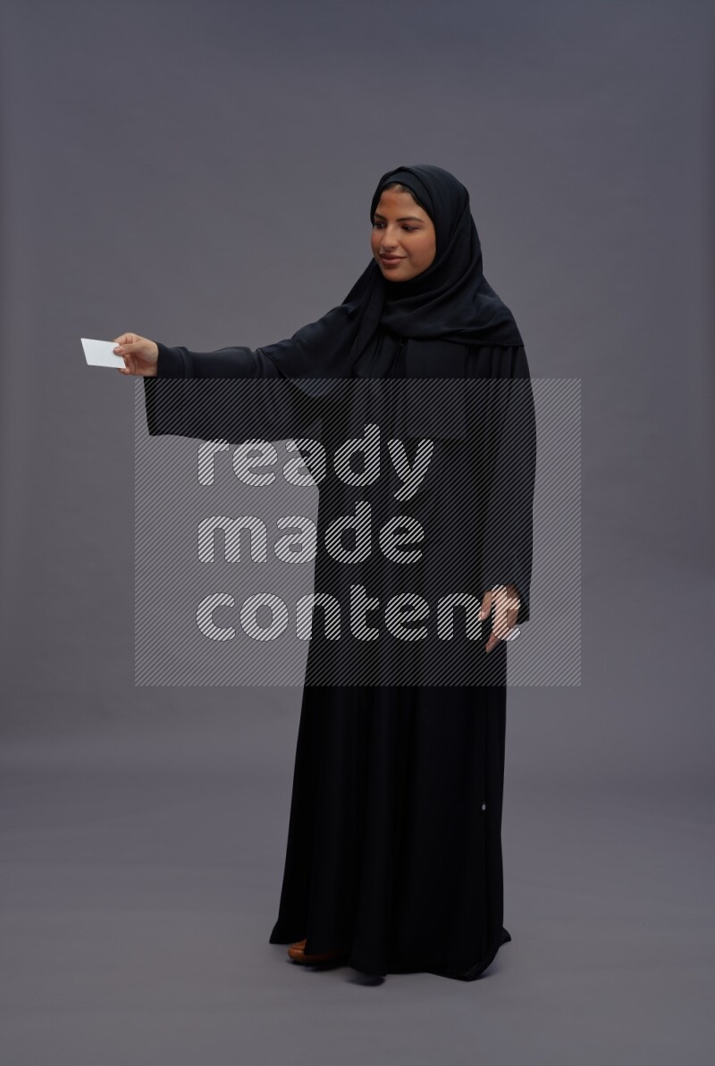 Saudi woman wearing Abaya standing holding ATM card on gray background
