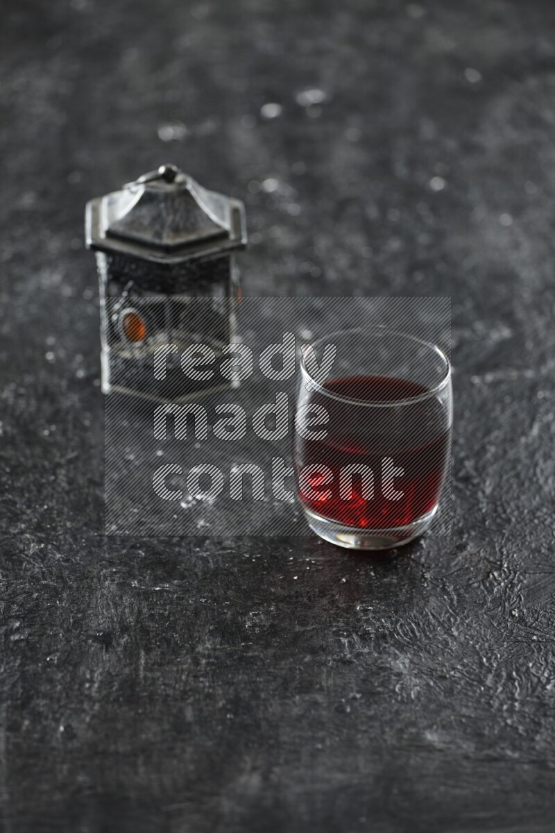A silver lantern with different drinks, dates, nuts, prayer beads and quran on textured black background