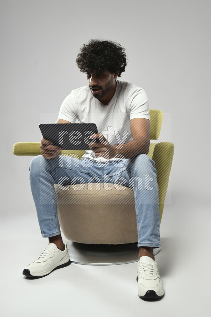 A man wearing casual sitting on a chair gaming on a tablet on white background