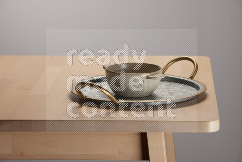 off white bowl placed on a rounded stainless steel tray with golden handels on the edge of wooden table