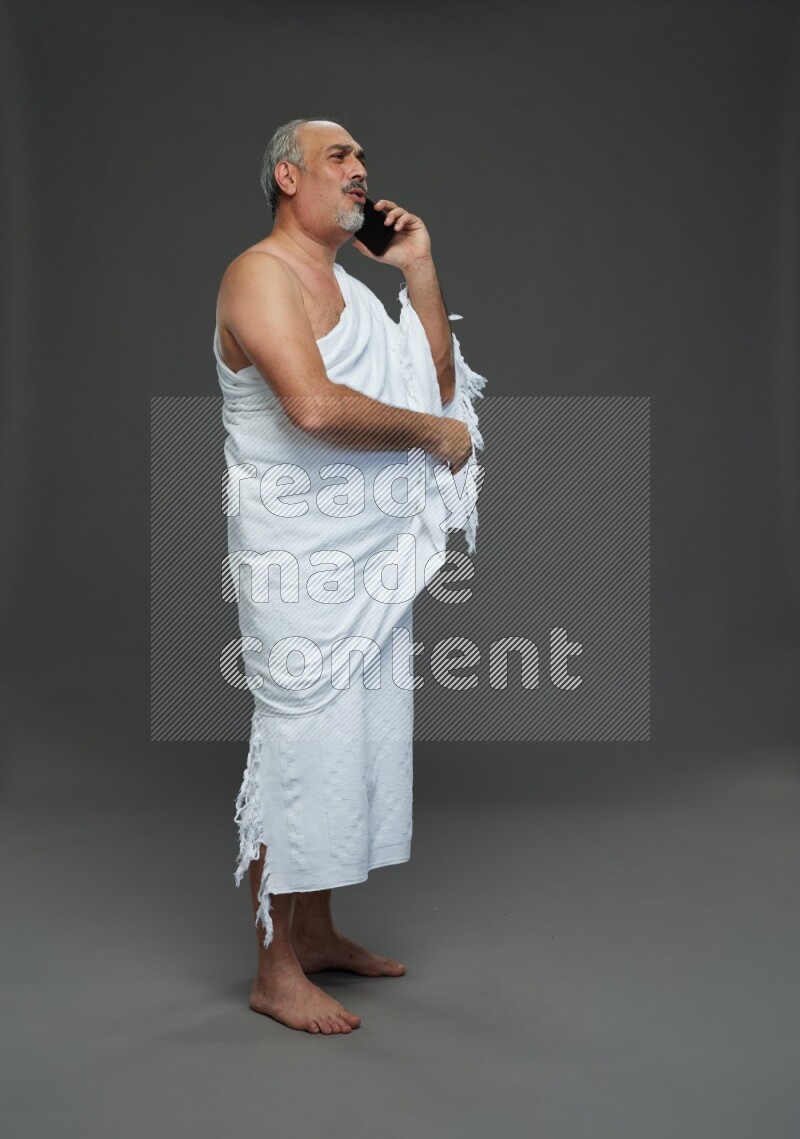 A man wearing Ehram Standing talking on phone on gray background