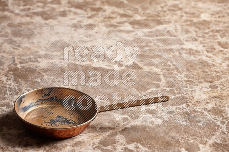 A small copper pan on beige marble background