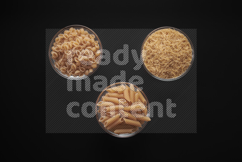 Different pasta types in glass bowls on black background