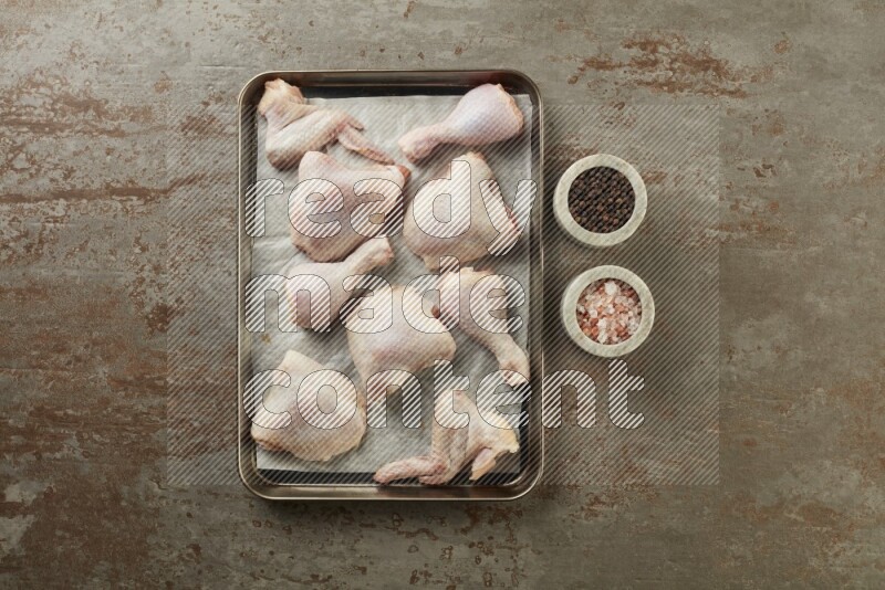 Mixed fresh chicken pieces in an oven tray on a textured rustic background