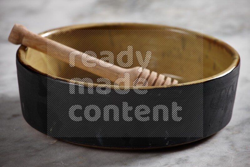 Multicolored pottery oven plate with wooden honey handle in it on grey marble background