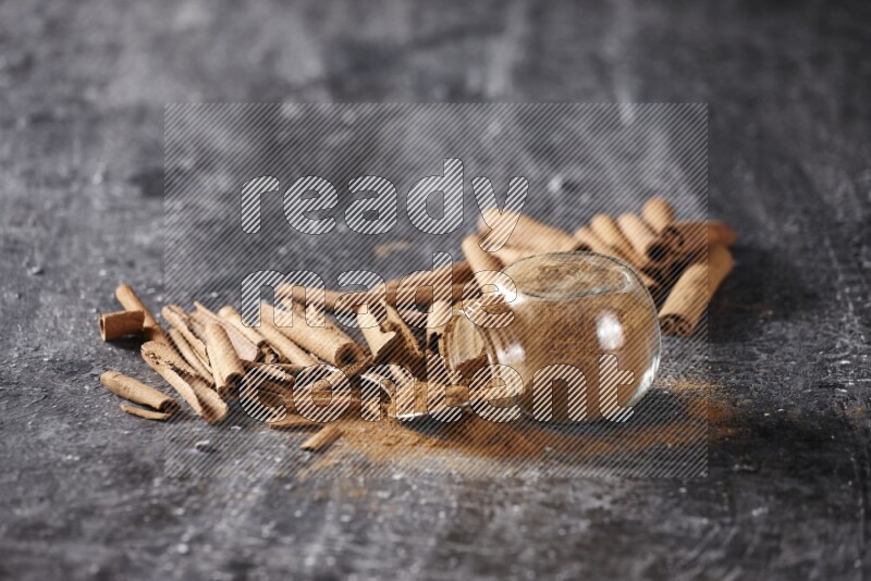 Herbal glass jar full cinnamon powder flipped and a metal spoon full of powder surrounded by cinnamon sticks on textured black background in different angles