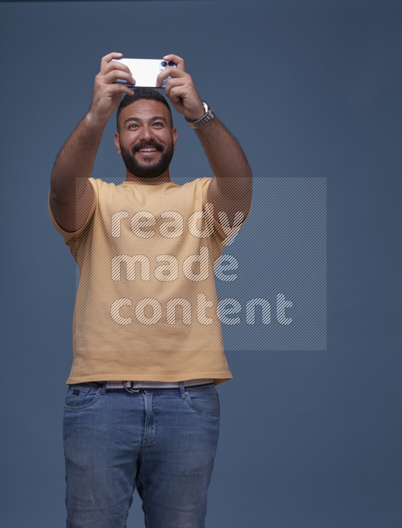 A man Playing Games on Smartphone on Blue Background wearing Orange T-shirt