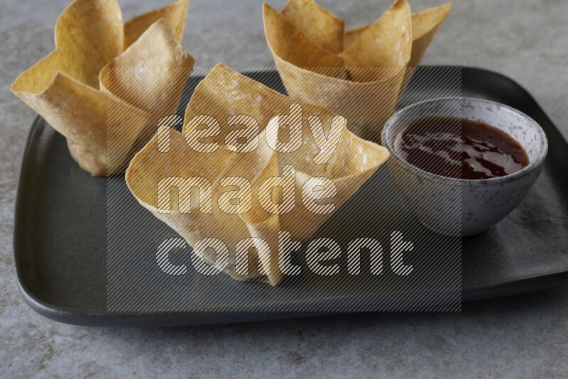 wonton cups with soy sauce ramkin on rectangle dark grey ceramic plate on grey textured counter top