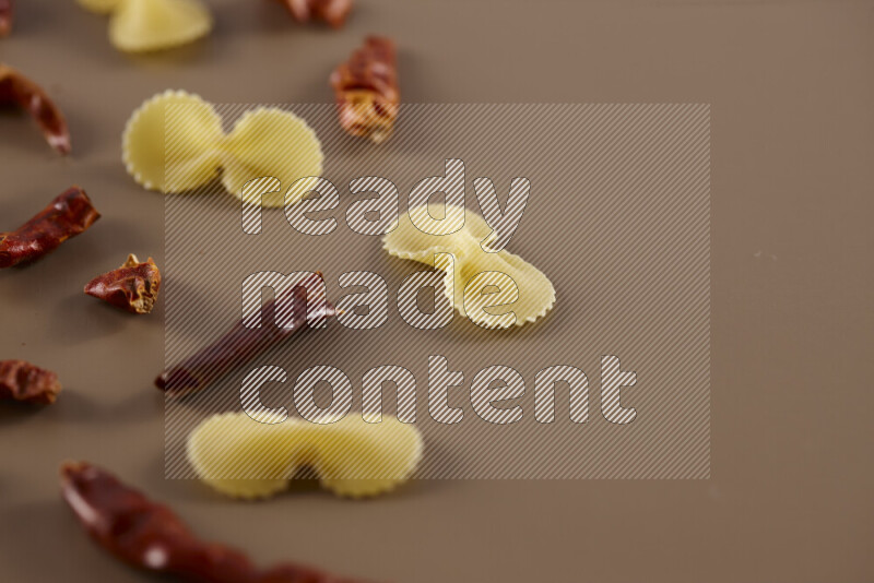 Raw pasta with different ingredients such as cherry tomatoes, garlic, onions, red chilis, black pepper, white pepper, bay laurel leaves, rosemary and cardamom on beige background